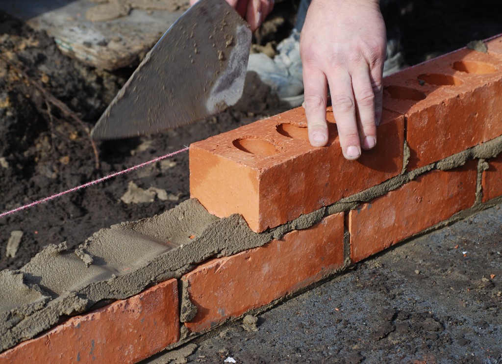 Construction worker laying bricks showing trowel and guideline.